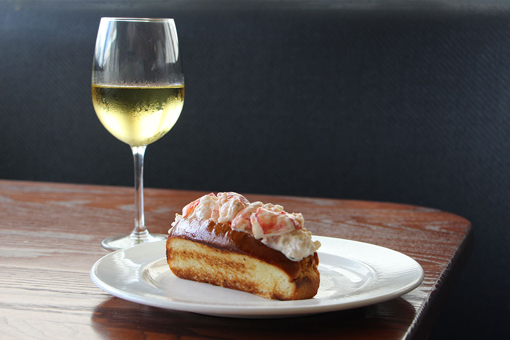 Lobster roll on a white plate paired with a blass of white wine.